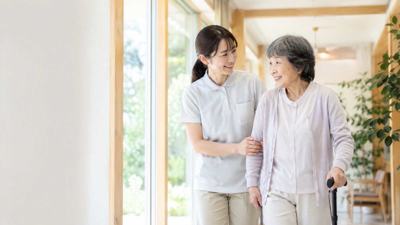 やさしい時間を、ホームページに。介護スタッフが利用者に寄り添って歩く様子。